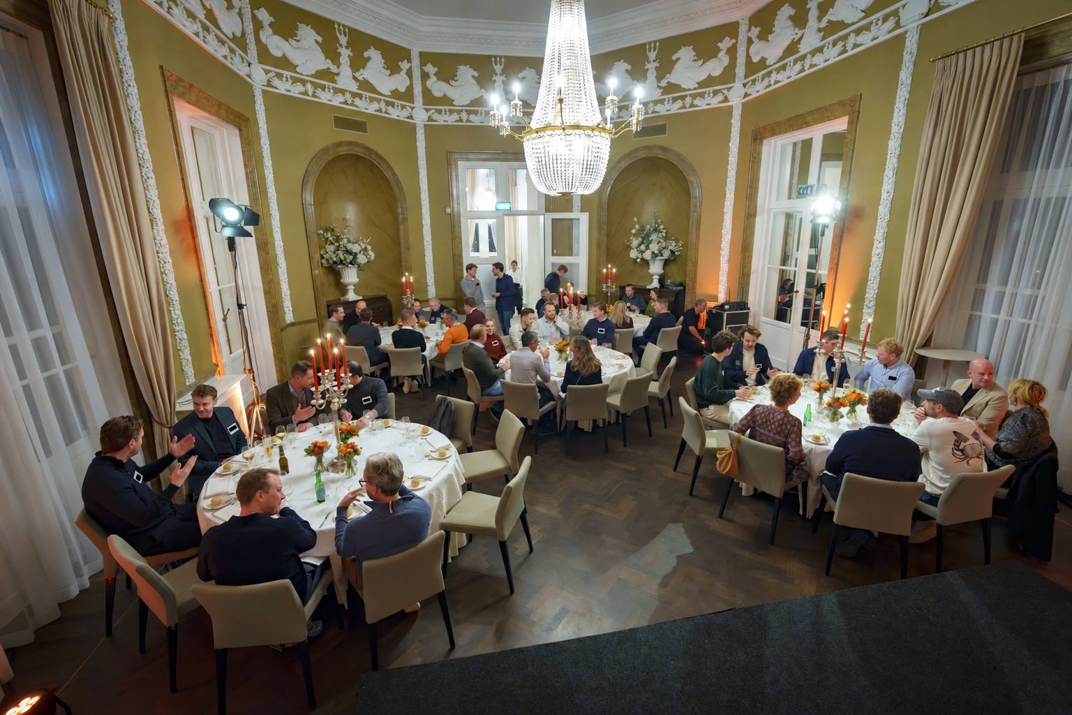Diner aan ronde tafels onder kroonluchters tijdens Connect